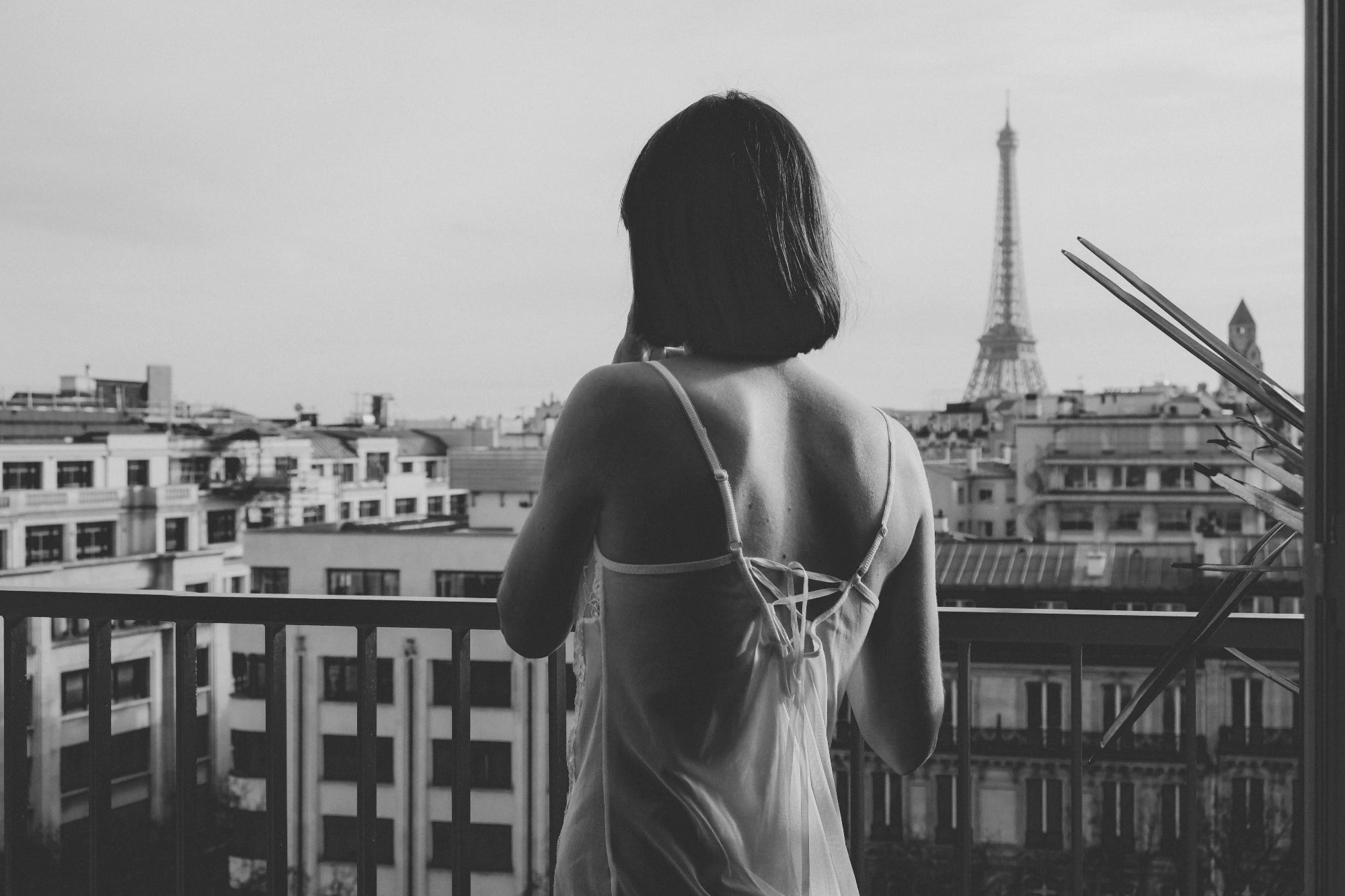 Woman standing on a balcony overlooking a cityscape with the Eiffel Tower in the background.